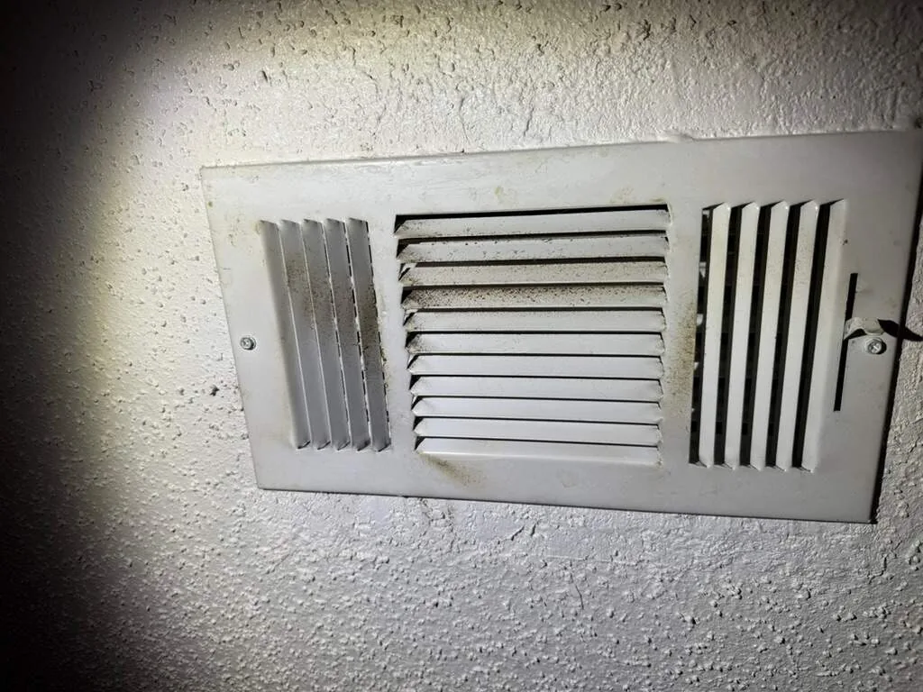 Dark residue along the louvers of a supply register in a home near an industrial fire