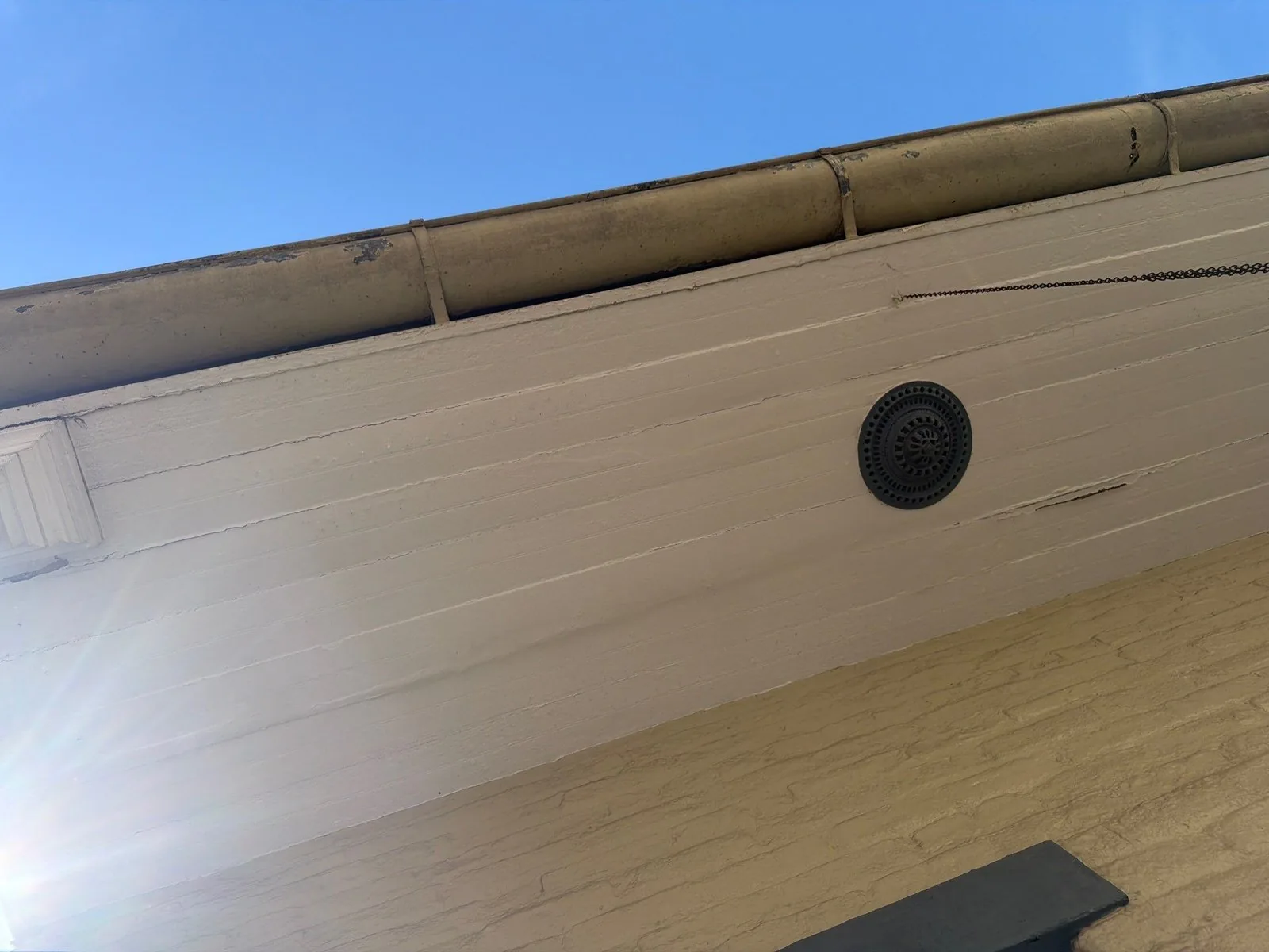 Looking up at the eave of an older house: gutter, trim and a round attic vent