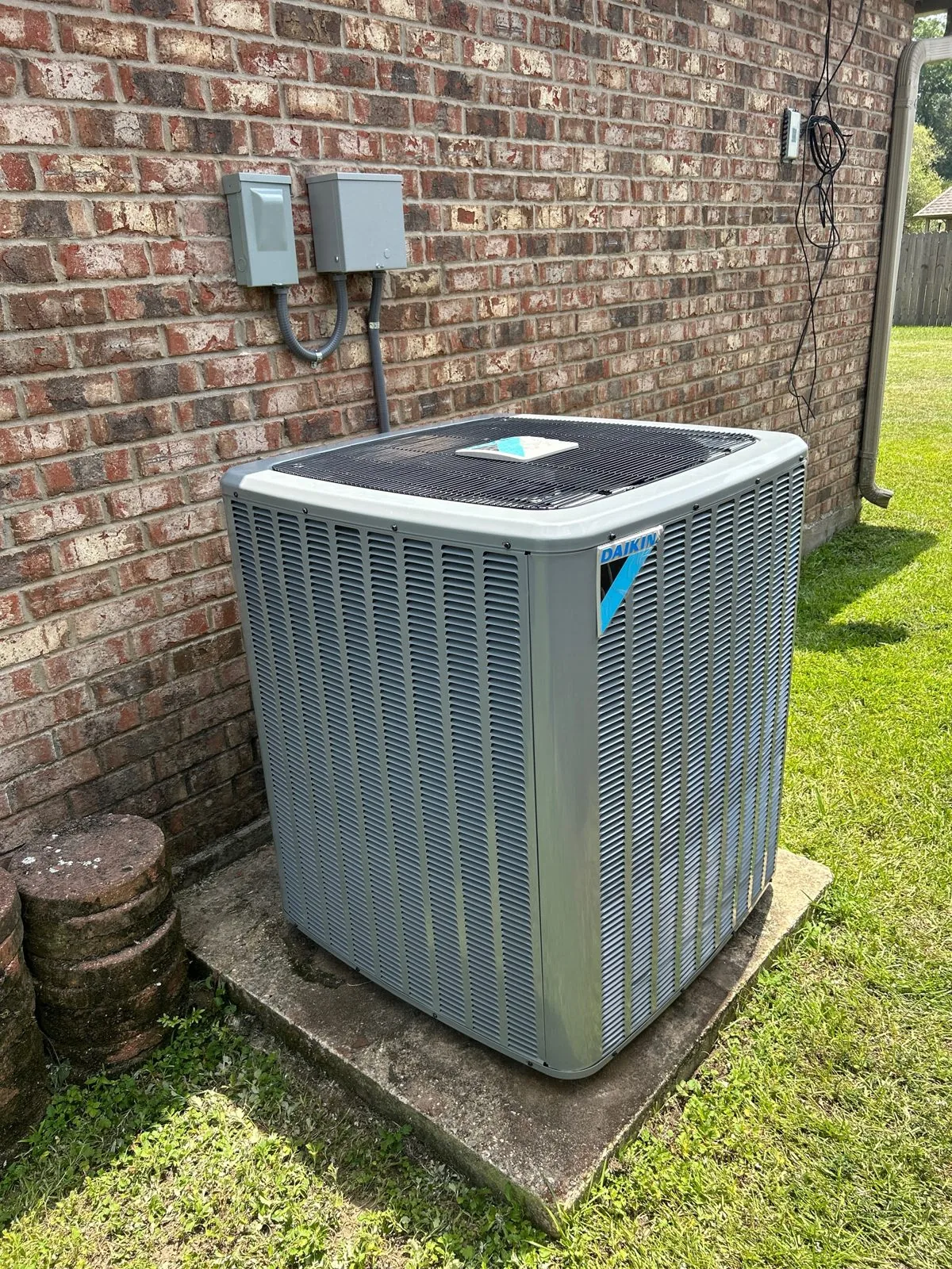 New Daikin condenser on a pad against a brick wall